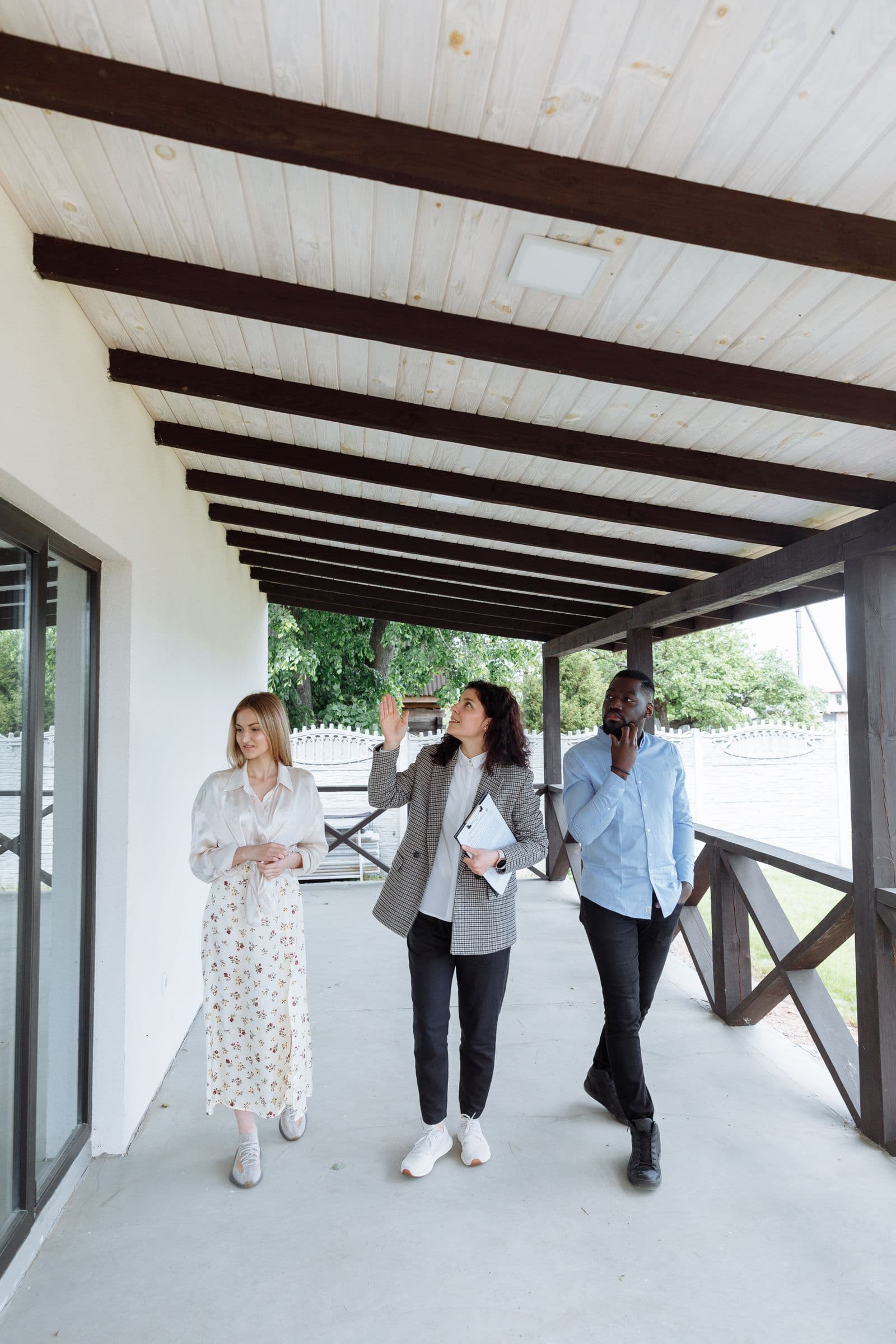 A real estate agent with a clipboard walking a couple along a covered porch