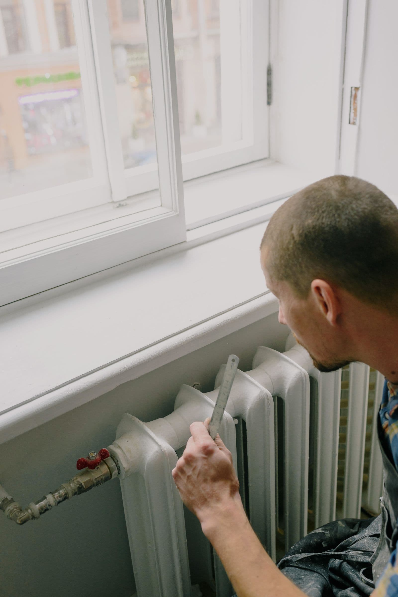 A heating technician measuring a radiator beside a window